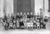 Foto av en skolklass med lärarinna, som samlats utanför skolans port.