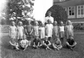 Foto av en skolklass med lärarinna, som samlats utanför skolan.
