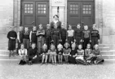 Foto av en skolklass med lärarinna, som samlats utanför skolans port.