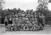 Foto av en skolklass med lärarinna, som samlats på skolgården.