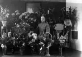 Foto av en man i uniform som sitter i ett vardagsrum, omgiven av blommor.