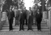 Foto av sju män i kostym som står på en trappa.