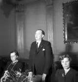 Sammanträde på Stadshotellet, 1943. 
En äldre man håller tal, stående mellan två sittande damer.