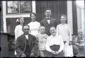 Porträtt av sju personer utanför en av byggnaderna i Stensjö by. Uppe från vänster Signe Karlsson, Märta Karlsson, Martin Karlsson och Judit Karlsson.
Sittandes är Karl Nilsson och Hilma Nilsson. Stående i mitten är Erik Karlsson.