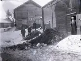 Vy över Stensjö bys uthuslängor vintertid. Det ligger snö på marken. En man och två pojkar står på en gödselstack. I mitten står Bengt Stensiö. Pojken till höger har ett gevär över axeln. Längst till höger i en dörröppning står en kvinna.