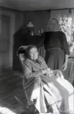 Porträtt av Titti Nilsson sittandes i en gungstol. Bakom henne står Emma Johansson.