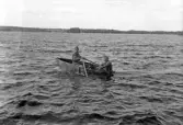 Foto av två militärer som ror en primitiv eka (jolle) på Helgasjön (?).