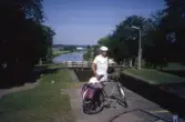 Man med cykel står vid Riksbergs sluss på Göta kanal, 1991