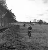 När våren kom, 1944. 
Orienteringsövning. En pojke är springande på väg över ett gärde.
I bakgrunden skymtar en bondgård m.m.