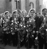 De första studenterna. 1944.
En grupp studenter vid Tegnérstatyn. Man verkar sjunga något. 
I bakgrunden skymtar en del av domkyrkan.