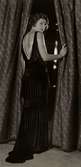 Nordiska Kompaniet, dammode. Kvinna vid draperi, iförd elegant aftonklänning med släp. NK:s franska damskrädderi den 19 mars 1930.