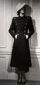 Dammode 1938, en kvinnlig modell poserar med en mörk dubbelknäppt kappa och hatt. Nordiska Kompaniet.
