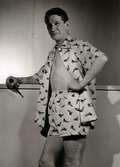 En man visar boxershorts och skjorta (möjligen pyjamas) i samma mönstrade tyg från California - Kläder. I handen håller han en pipa. På varuhuset Nordiska Kompaniet i Stockholm 1947.