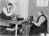 Björcks skrädderi i Söraby år 1924-25. SKräddarmästaren själv  vid symaskinen, mågen på bordet vid pressjärnet. Småland, Söraby. 