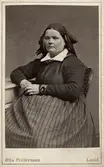Porträtt av sittande kvinna iklädd huvudduk och randigt förkläde. Knästorp, Bara hd. Gåva från fotograf O. Pettersson i Lund, 1873. 