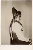 Porträtt i profil av kvinna klädd i folkdräkt från Dalarna som sitter på en stol.