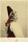 Porträtt på en kvinna i folkdräkt från Dalarna med toppig huvudbonad. Handkolorerat ateljéfoto.
