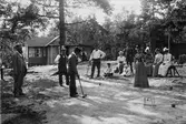 Män och kvinnor spelar krocket framför hus på Lidingö. 