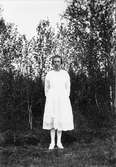 Stående flicka med vita kläder i en skogsglänta