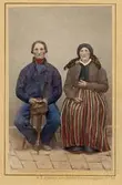 Ett par poserar sittande klädda i folkdräkter, Gummarp, Glimåkra socken, Göinge härad i Skåne. Kolorerat i efterhand. Inv.nr. 18536a.