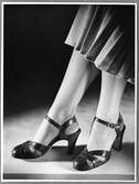 Skomodet 1948 visas av kvinnlig modell. I bild endast kvinnans fötter och ben, hon bär ett par sandaletter med vristrem, flätad tåkappa och halvhög klack. Hon har tunna strumpor med fotförstärkning och en plisserad kjol..