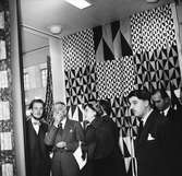 NK, utställningen Signerad textil har vernissage 29 oktober 1954. Till vänster i bild står Olle Bonniér och Stellan Mörner, till höger i förgrunden Olle Baertling. I bakgrunden tyger som de har formgivit.