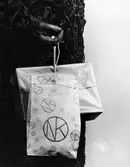 Påsar med NK:s logotyp. Närbild på påsar från Nordiska Kompaniet i Stockholm. En kvinna iklädd persianpäls och handskar håller två påsar i handen. Mars 1941