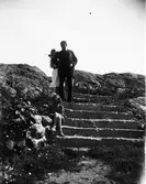 Man och två flickor på stentrappa vid strand. Troligen i Fiskebäckskil, Bohuslän.