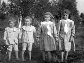 Gruppbild av fyra barn. Två pojkar i likadana randiga dräkter med sjömanskrage och korta byxor. Två flickor i likadana rutiga klänningar med vita kragar.
