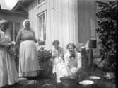 Fyra kvinnor utanför ett hus. Den ena diskar i en balja och de andra hjälper till.