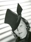 Porträtt av kvinna med hatt i filt från Marie Alphonsine. Randigt ljusmönster i bakgrunden.
