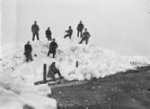 Isvinter. En grupp män står och sitter på en imponerande hög med isflak.