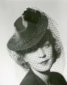 Porträtt av kvinna i hatt med svart dekoration och flor.