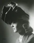 Porträtt av kvinna i hatt med veck och flor.