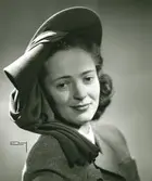 Porträtt av kvinna med hatt i grön filt med garnityr av brun jersey. Hatt använd vid franska avdelningens uppvisning september 1947.