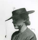 Fb, Porträtt av kvinna i hatt med flor och nål med kula.