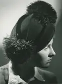 Porträtt av kvinna i dunkelbrun velourhatt med pompons av strutsfjädrar. Modell från Maison Blanche & Simone.