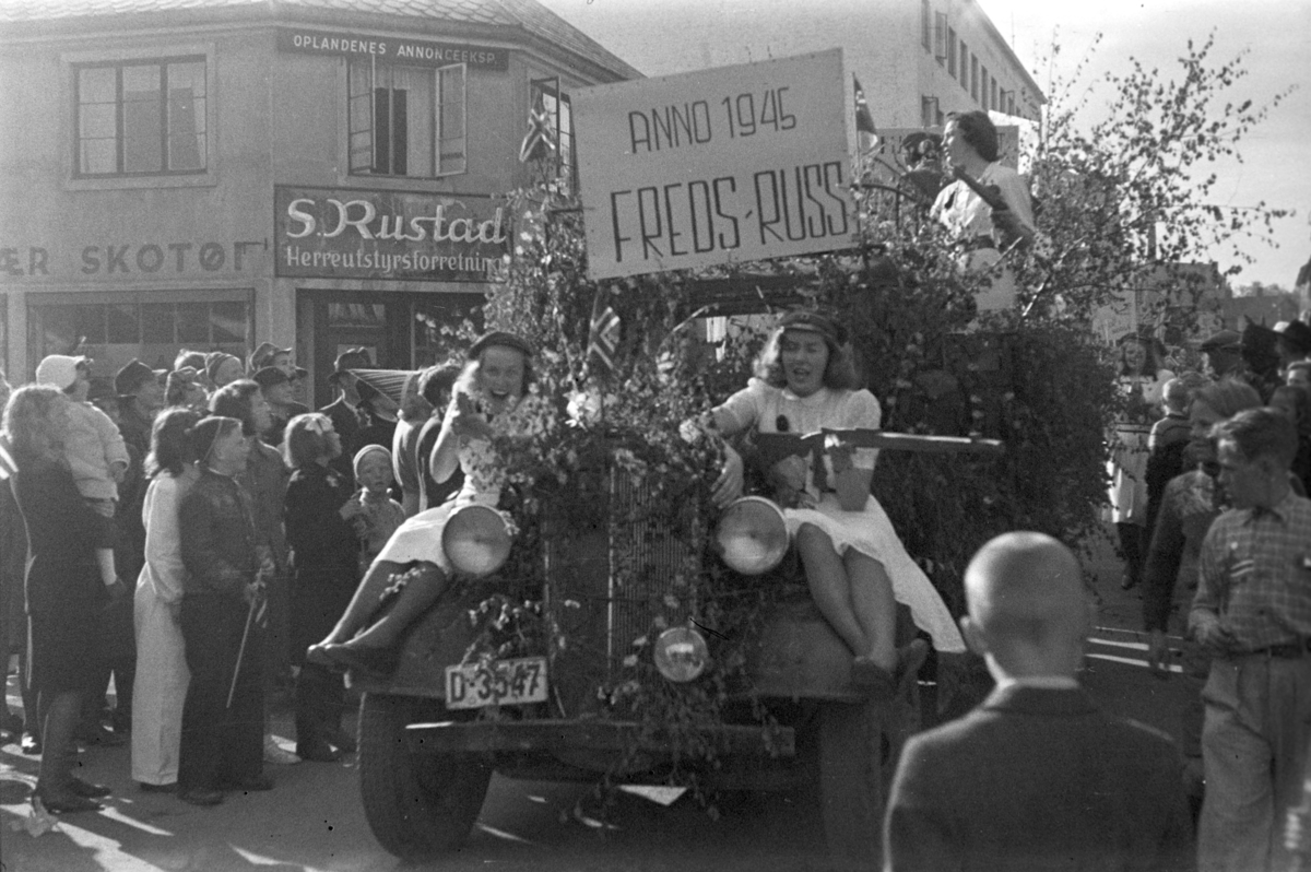 17. mai 1945. Hamar. Nasjonaldag. Frigjøringen. Russetoget passerer forbi S. Rustads forretning i Torggata 42. Fredsdagene. Plakat "Fredsruss anno 1945. "