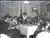 Gruppbild, tio kvinnor sittande vid ett dukat kaffebord. En serverar och några dricker kaffe. Ateljébild. Beställare:Hilda Johansson.