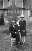 Familjeporträtt av Gunnar Dal, hans hustru Alice och dotter Maj fotograferade i en trädgård framför en bostad i Galtabo, Drängsered. . Hustru Alice har en hatt.