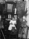 Liten flicka med hund som sitter på en stol. 1900-tal. Inomhus.
