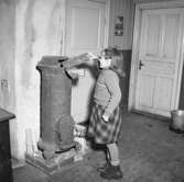 Skolflicka eldar i klassrummets kamin i skola på landsbygden år 1947