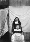 Fotografering av två barn medan ett tredje hjälper till att hålla upp bakgrunden, antagligen två vita lakan.