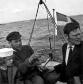 Skrivet på vidhängande papper: På väg från Bäckviken till Kyrkbacken.
Axel Gustafsson med dotter och Nils Nilsson.
Fotot är taget: 1965-06-09