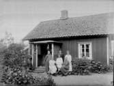Fyra äldre kvinnor och två pojkar (en i sjömanskostym) poserar framför ett bostadshus.