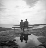 Kvinna och man sitter på en bänk och skådar ut över havet