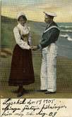 Postkort. En kvinna i folkdräkt och en man i sjömanskostym står på en strand och håller varandra i hand
