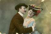 Kolorerat postkort föreställande en man som håller om en kvinna, mannen försöker kyssa kvinnan som tittar mot betraktaren