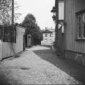 Kullerstensgata i Jönköping. Till vänster plank och mitt emot trähusfasader med en väggfast gatlykta.