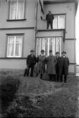 Fem män står framför ett hus, den sjätte står på taket på liten utbyggnad.